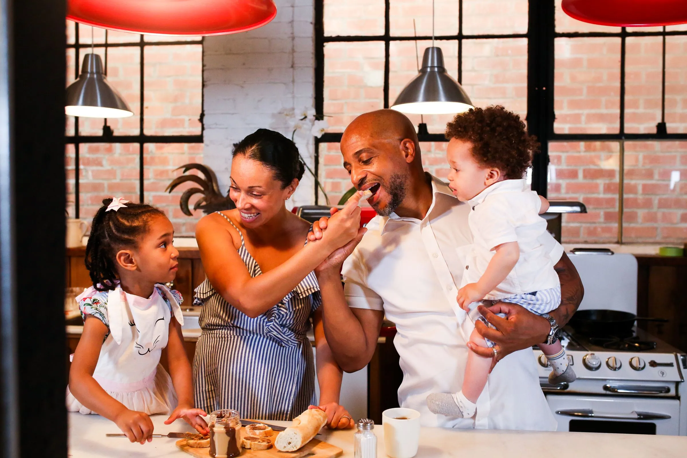 A family laughing together while cooking in a brick-walled home kitchen
