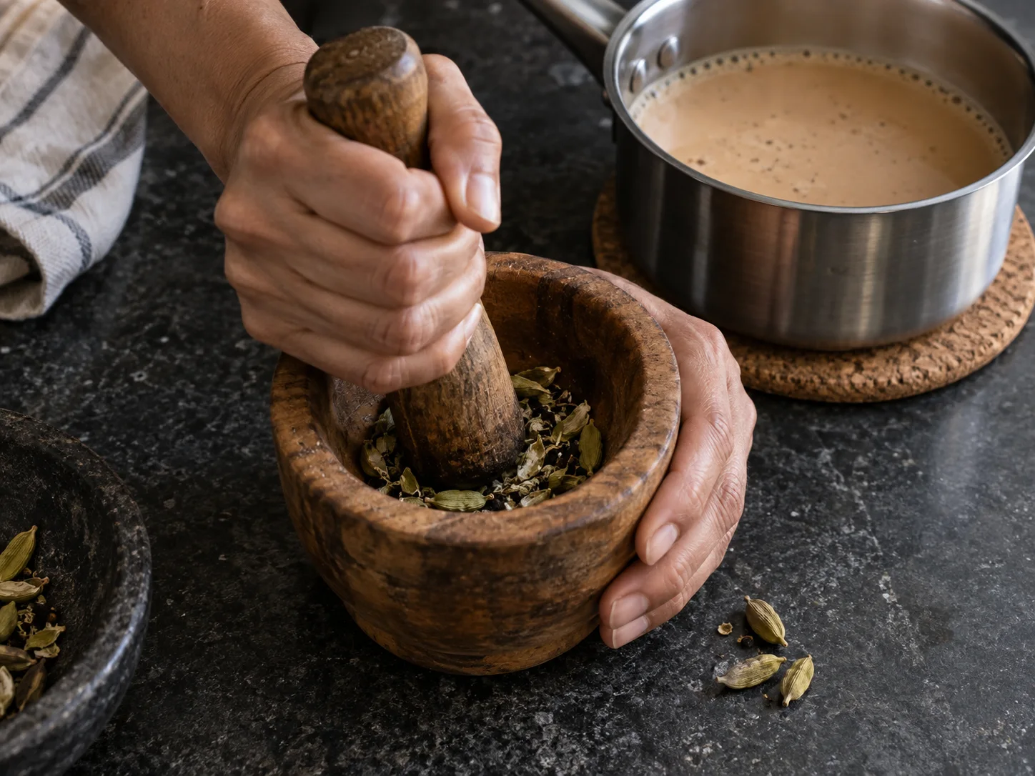Hands lightly crushing green cardamom pods for chai