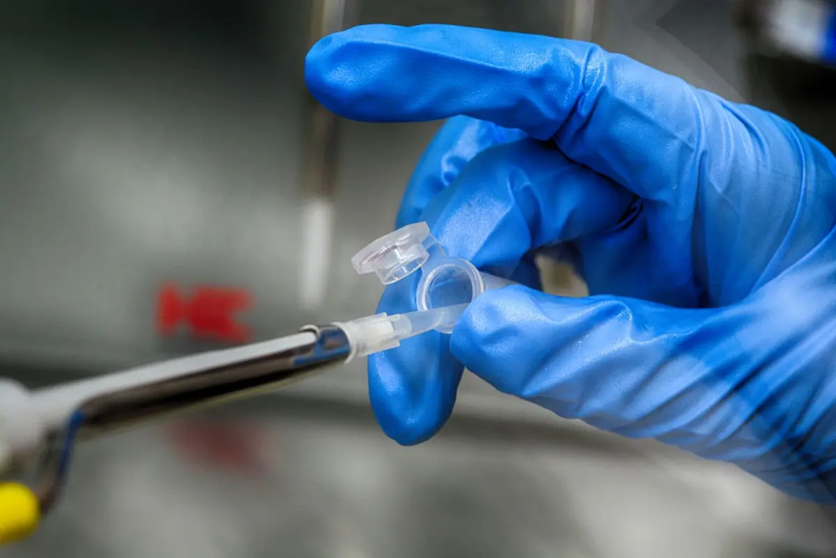 Close-up photograph of gloved hands handling a sample tube and testing equipment